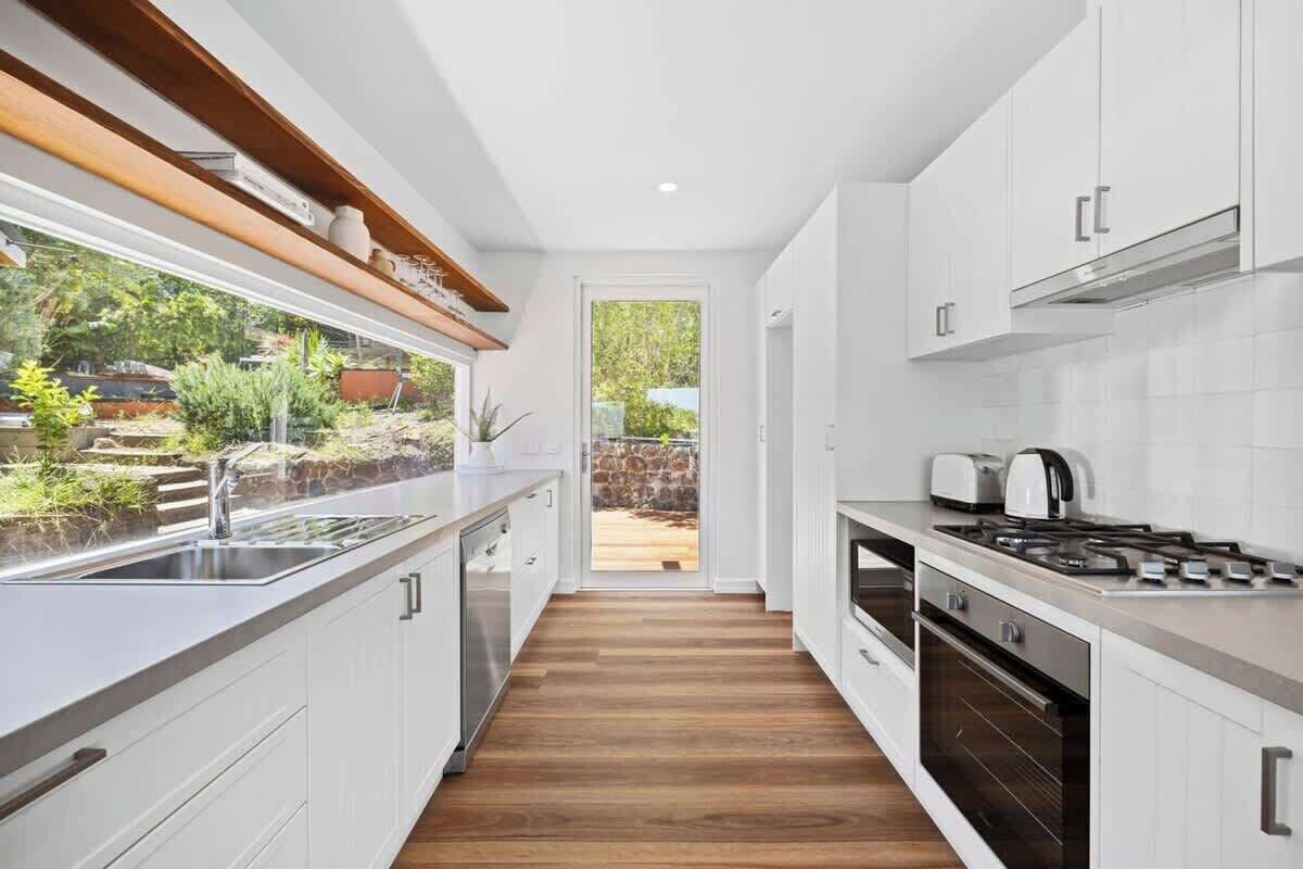 Una cocina moderna con armarios blancos, un lavamanos de acero inoxidable y vistas a un jardín.