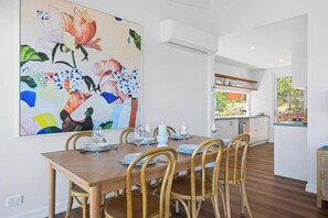 A dining area with a wooden table set for four, surrounded by wooden chairs. A large abstract painting adorns the wall above the table.