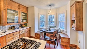 A kitchen with wooden cabinets, a gas stove, and a dining table with chairs. - Bloomington Bungalow - Steps to Campus! (Bloomington)