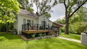 A two-story house with a front deck, a staircase leading to the deck, and a small garden area. - Bloomington Bungalow - Steps to Campus! (Bloomington)
