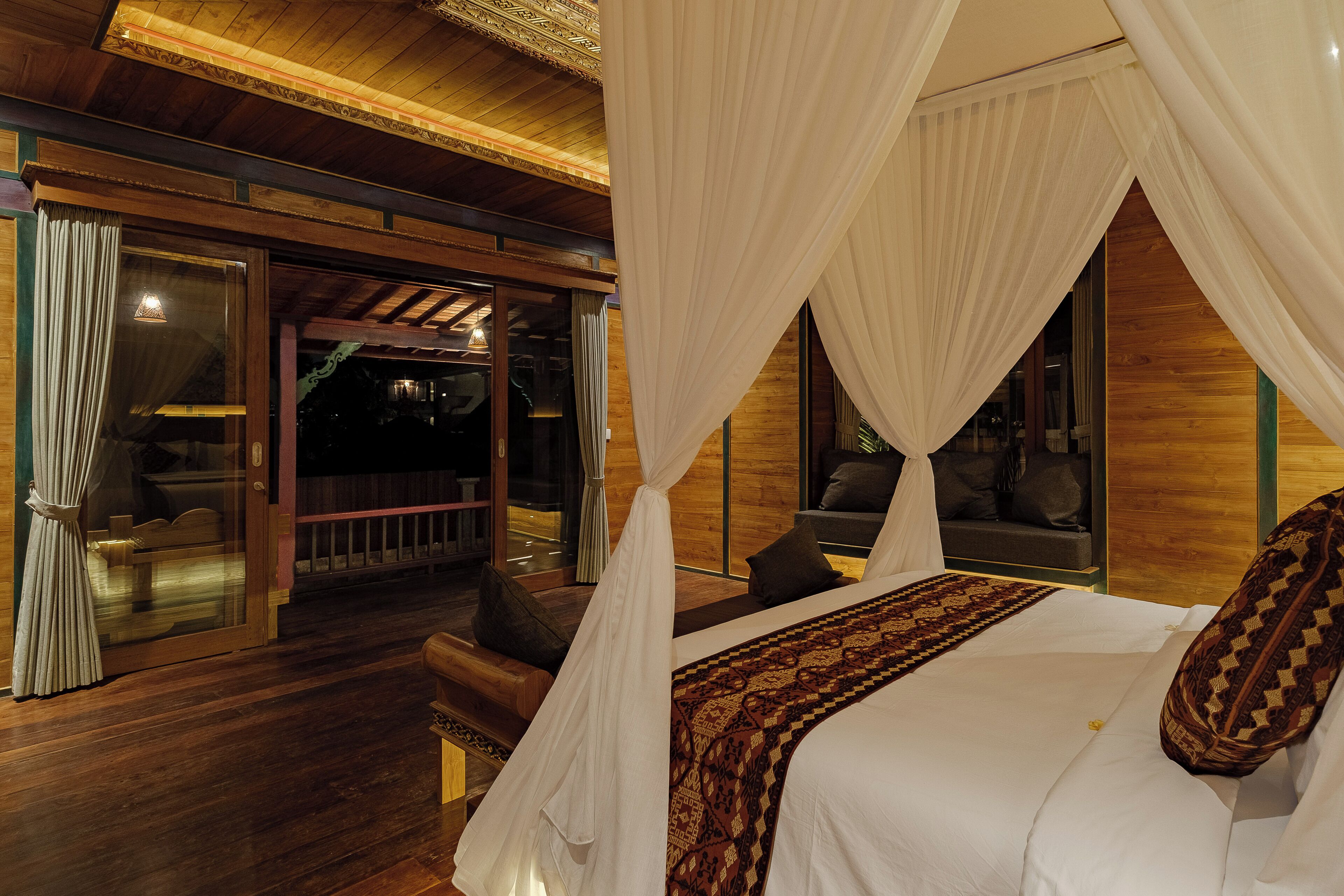 A bedroom with a canopy bed, wooden flooring, and a view of the outside.