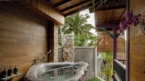Una bañera de piedra en una habitación de madera con pared de piedra y un pequeño jardín.