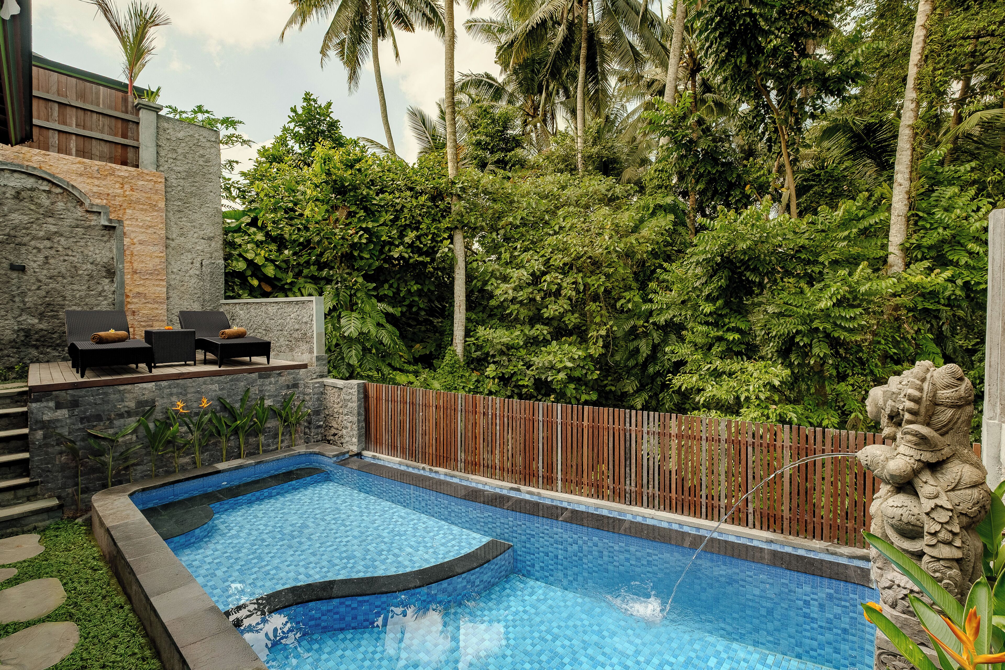 A swimming pool with a stone wall and a wooden deck with lounge chairs.