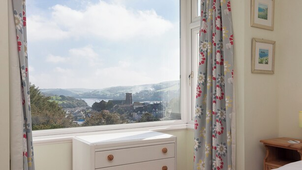 Een slaapkamer met uitzicht op een stad en heuvels, een witte dressoir en een groene sprei.