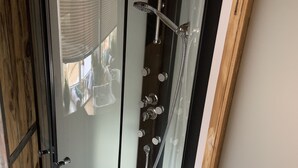 Et brusebad med glasvægge, hvidt gulv, håndbruser og armatur på væggen.