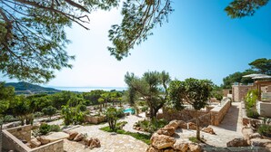 Eine Steinterrasse mit Pool, umgeben von Bäumen und Blick auf das Meer.
