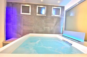 Une salle de bain moderne dotée d’une grande baignoire, d’un espace douche et de trois écrans fixés au mur.