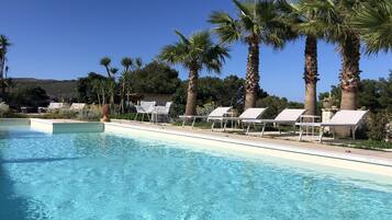 Relax by the serene pool surrounded by palm trees and lounge chairs.