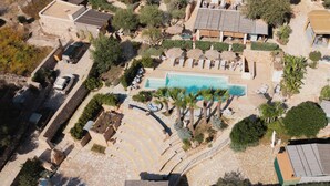 Eine Vogelperspektive zeigt einen Urlaubsort mit einem Schwimmbad, Liegestühlen und einem Kiesweg, der zum Pool führt.