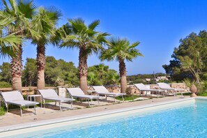 Un espace aménagé au bord de la piscine, avec des chaises longues et des palmiers.