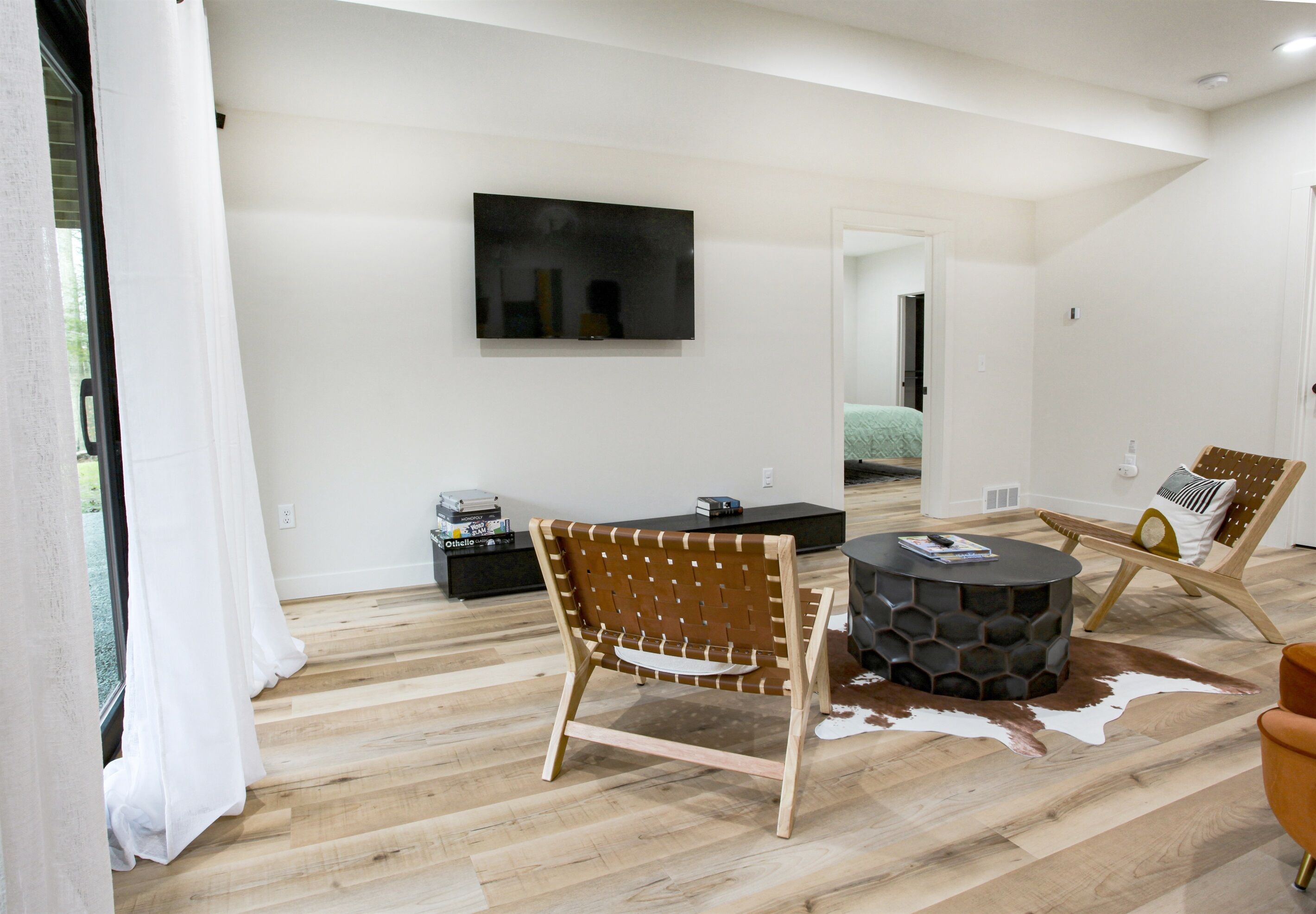 A modern living room with a wooden floor, a round coffee table, a leather sofa, and a TV mounted on the wall.