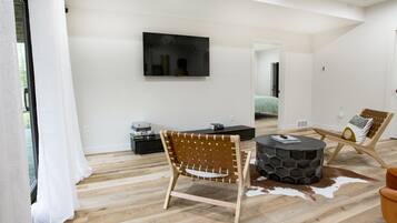 A modern living room with a wooden floor, a round coffee table, a leather sofa, and a TV mounted on the wall.