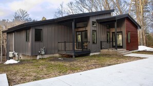 A modern two-story house with a covered porch, large windows, and a red accent wall. - Serene Retreat Awaits: Welcome to Endless Views,Your Luxurious Contemporary Home (Muskegon)