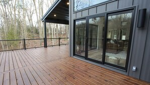 A wooden deck with a glass door leading to a room with a sofa and a basket. - Serene Retreat Awaits: Welcome to Endless Views,Your Luxurious Contemporary Home (Muskegon)