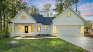 A two-story house with a garage, a front porch, and a well-maintained lawn. - Enjoy a modern Lake Sinclair retreat with two king beds, a private putting green, kayaks, and a game room. (Sparta)