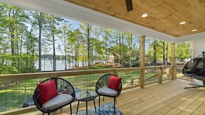 A wooden deck with two chairs and a hanging chair overlooking a lake. - Enjoy a modern Lake Sinclair retreat with two king beds, a private putting green, kayaks, and a game room. (Sparta)