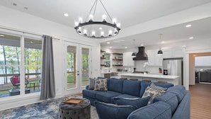 A modern living room with a blue sofa, ottoman, and a chandelier. - Enjoy a modern Lake Sinclair retreat with two king beds, a private putting green, kayaks, and a game room. (Sparta)