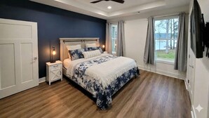 A bedroom with a bed, bedside tables, a ceiling fan, and a window with curtains. - Enjoy a modern Lake Sinclair retreat with two king beds, a private putting green, kayaks, and a game room. (Sparta)