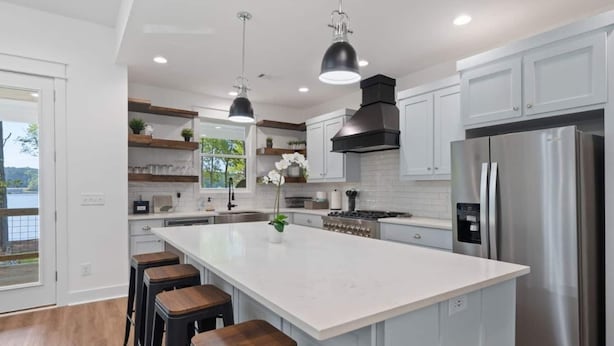 A modern kitchen with a large island, stainless steel appliances, and wooden bar stools. - Enjoy a modern Lake Sinclair retreat with two king beds, a private putting green, kayaks, and a game room. (Sparta)