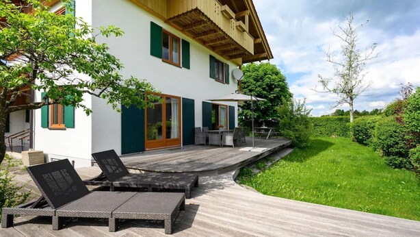 Ett modernt hus med en träaltan, utomhusmöbler och en välskött trädgård.