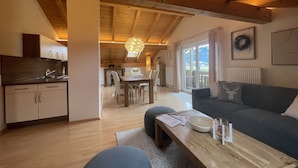 A spacious living area with a wooden ceiling, a dining table with chairs, a sofa, and a view of a mountain through large windows. - Birkeneck 1 (DG), castle view dream holiday apartment (Schwangau)