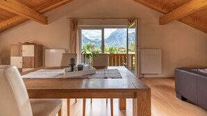 A spacious room with a wooden ceiling, a large window offering a mountain view, a dining table with chairs, and a sofa. - Birkeneck 1 (DG), castle view dream holiday apartment (Schwangau)