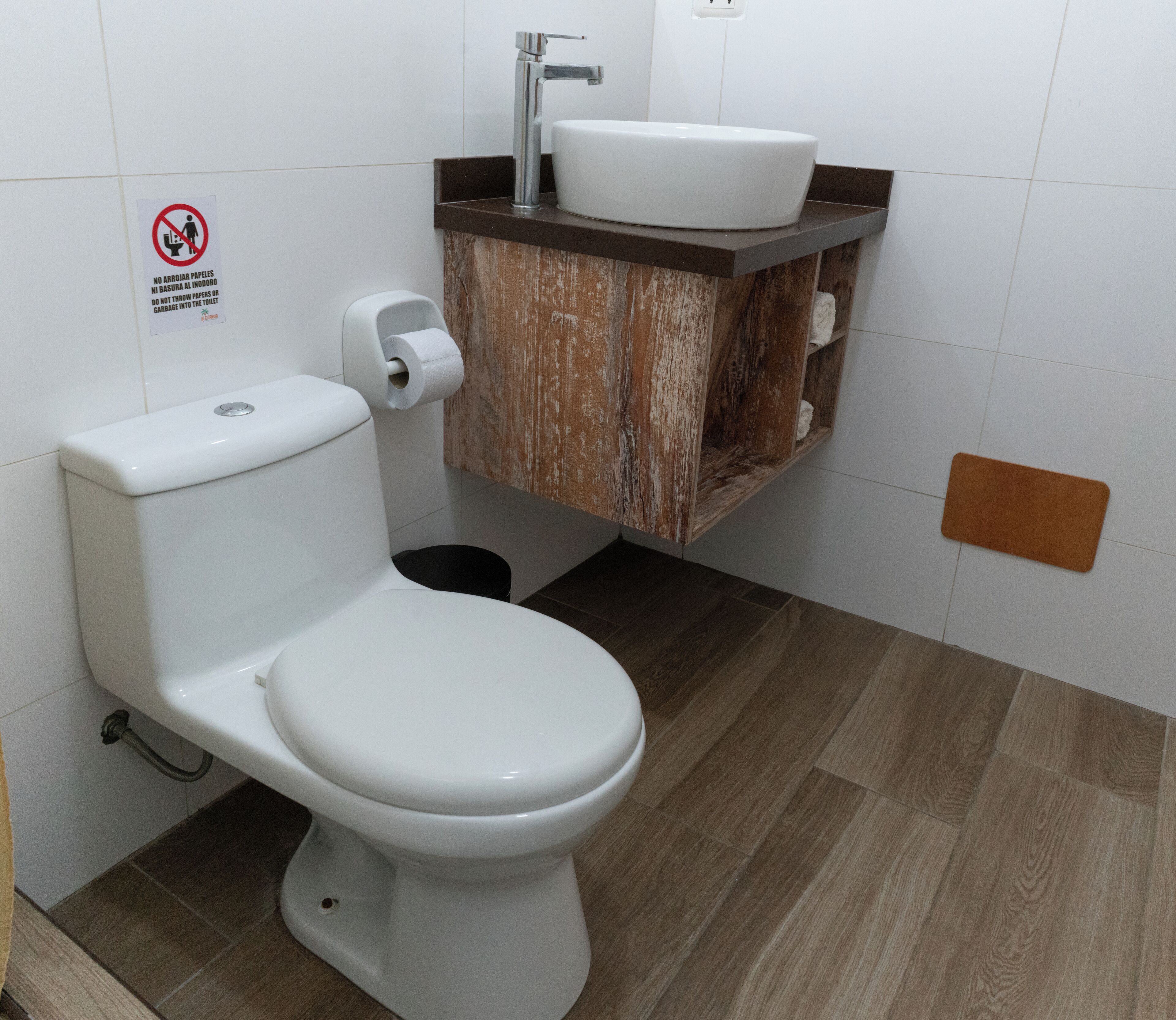 A bathroom with a white toilet, a wooden vanity with a sink, and a toilet paper holder.