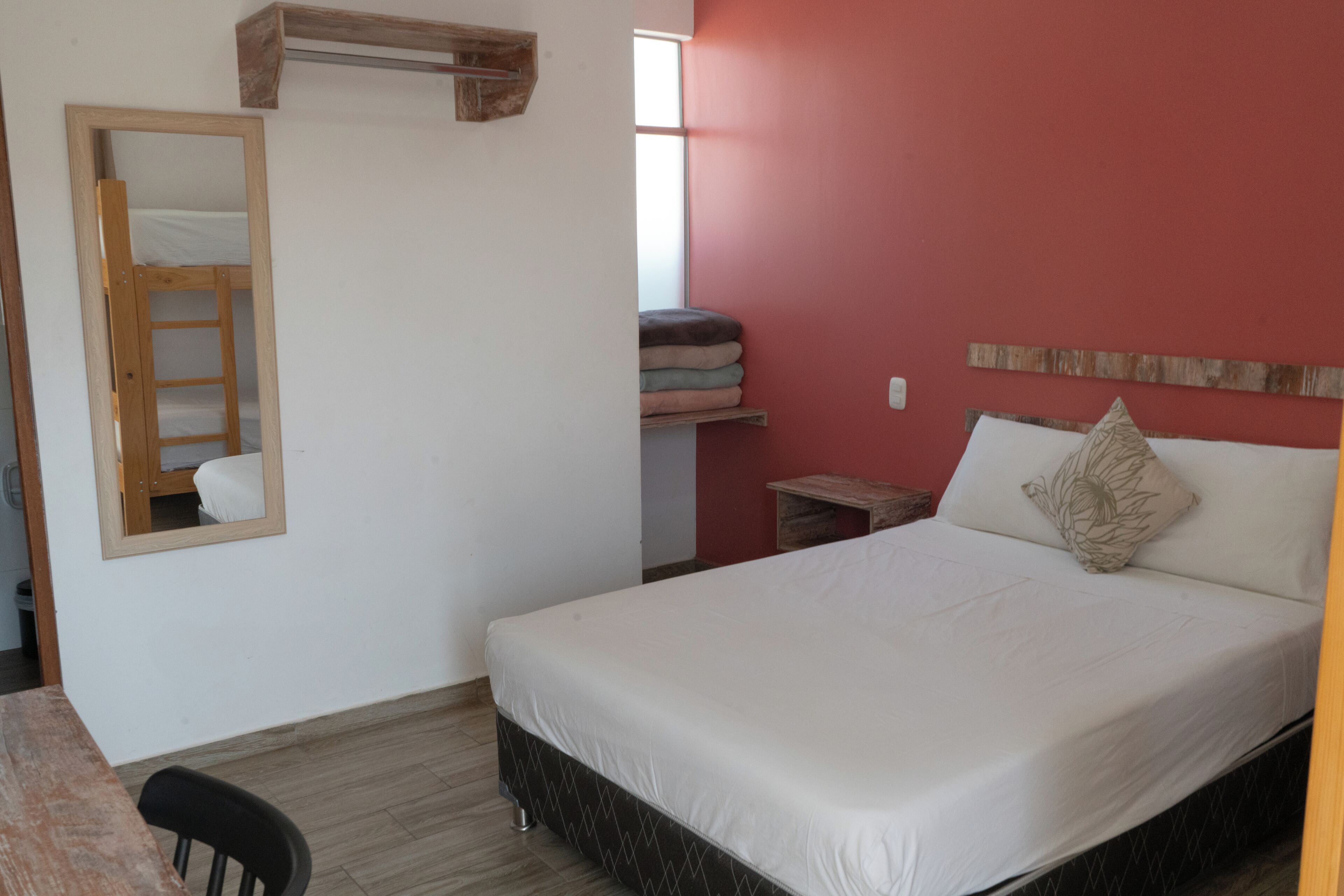 Un dormitorio con una cama, una silla, un estante de madera y una ventana.