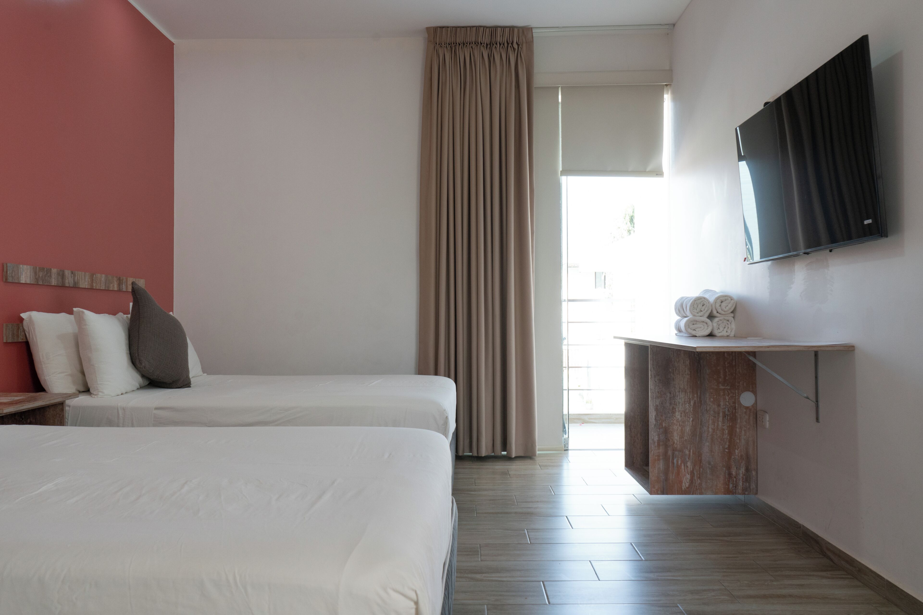 Une chambre d’hôtel avec deux lits, une télévision, une armoire en bois contenant des serviettes et une vue sur l’extérieur.