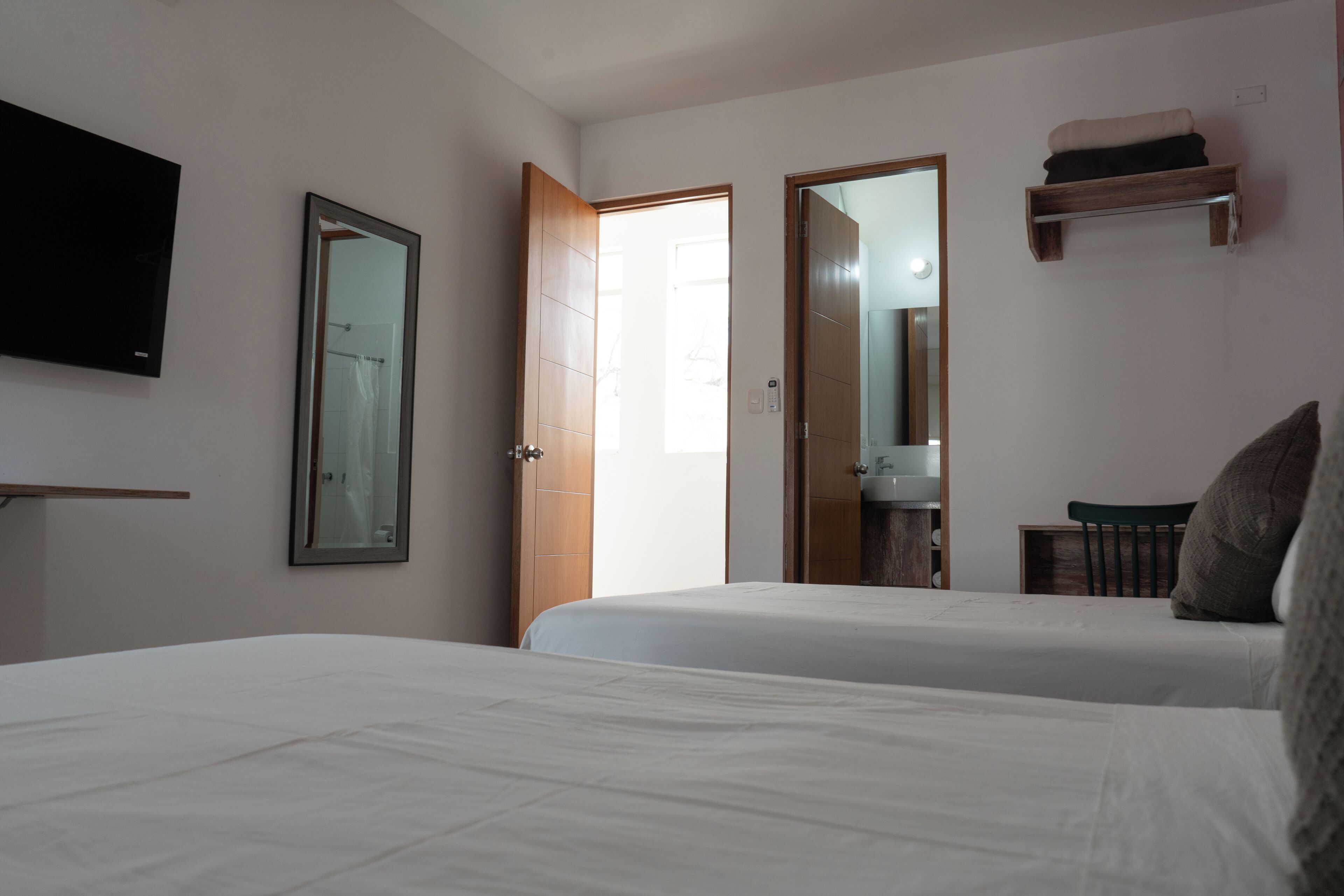 A bedroom with two beds, a TV, a mirror, and a bathroom visible through an open door.