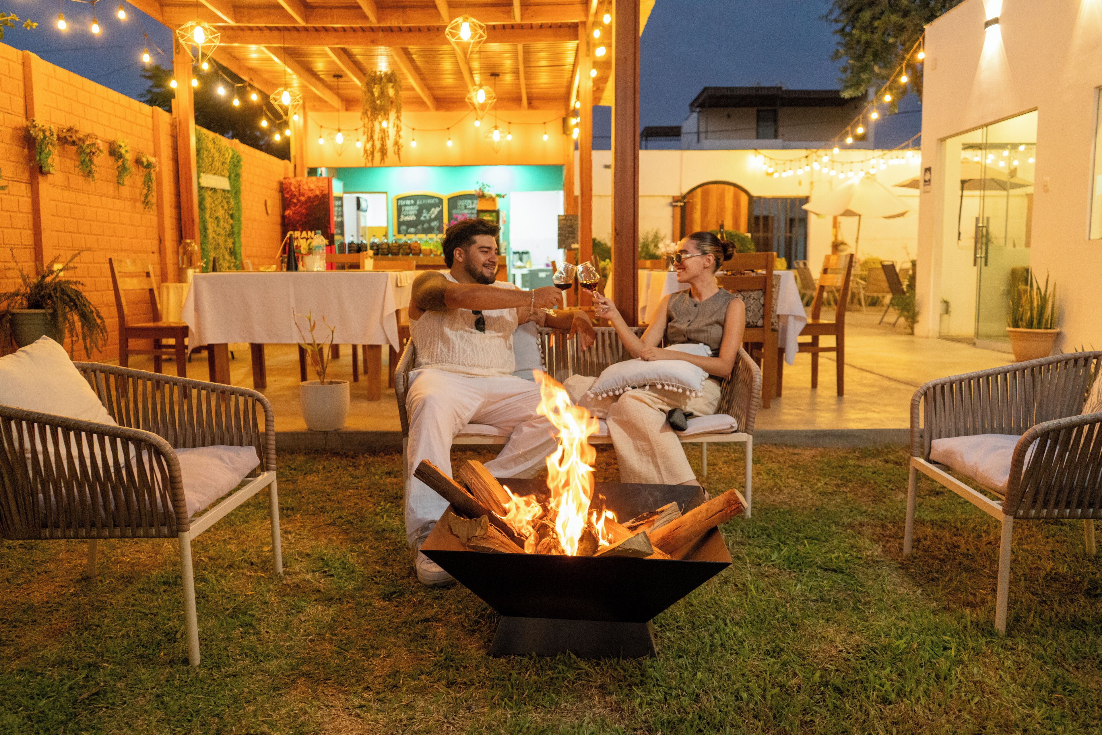 Un patio con una fogata, asientos al aire libre y luces colgantes.