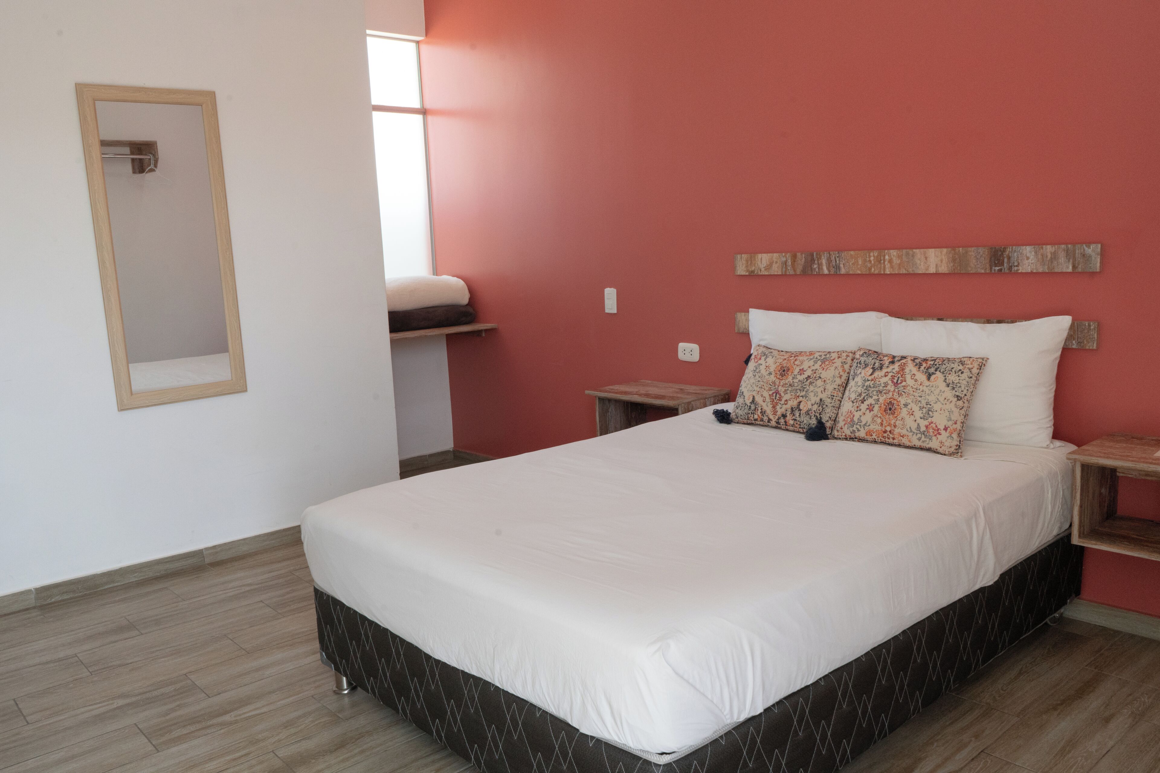 Un dormitorio con cama, mesita de noche, espejo y ventana.