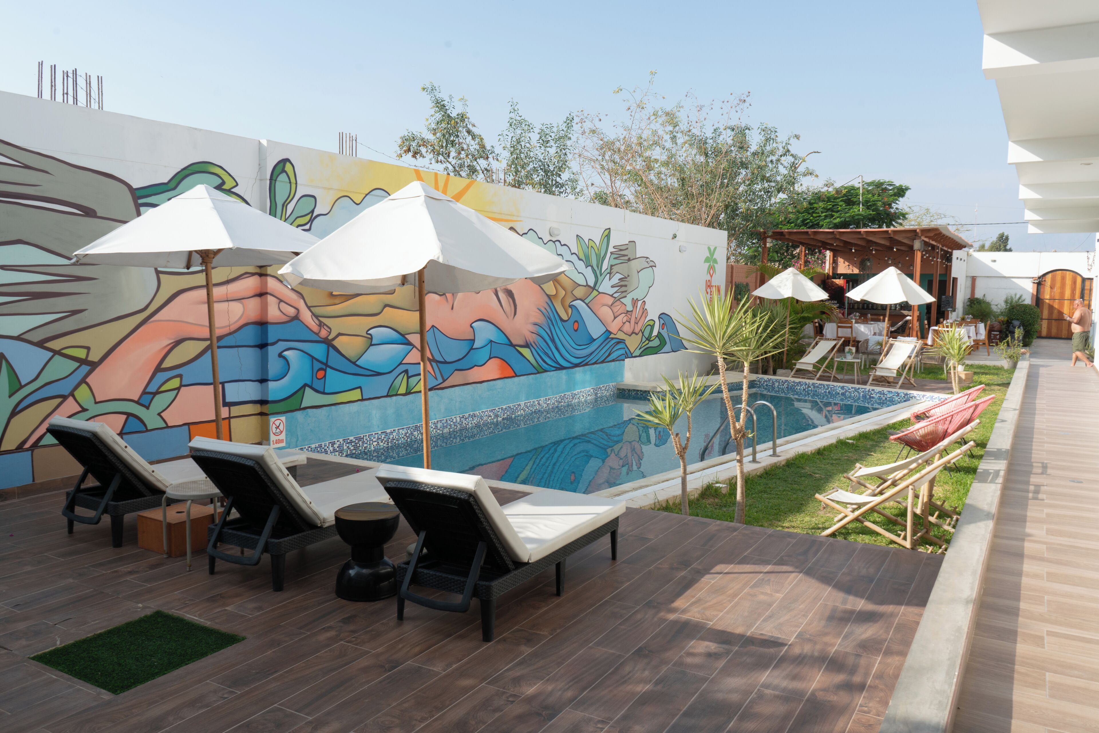 Un área junto a la piscina con sillones de descanso, sombrillas y un mural.