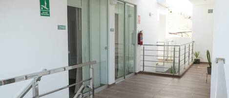 Corredor moderno de hotel com portas de vidro, um extintor de incêndio e plantas em vasos.