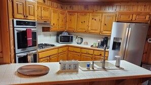 A kitchen with wooden cabinets, a stainless steel refrigerator, a microwave, and a wooden island with a cutting board.
