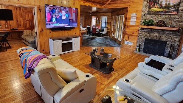 A spacious living room with wooden floors, a stone fireplace, a television, and a seating area with sofas and a coffee table.