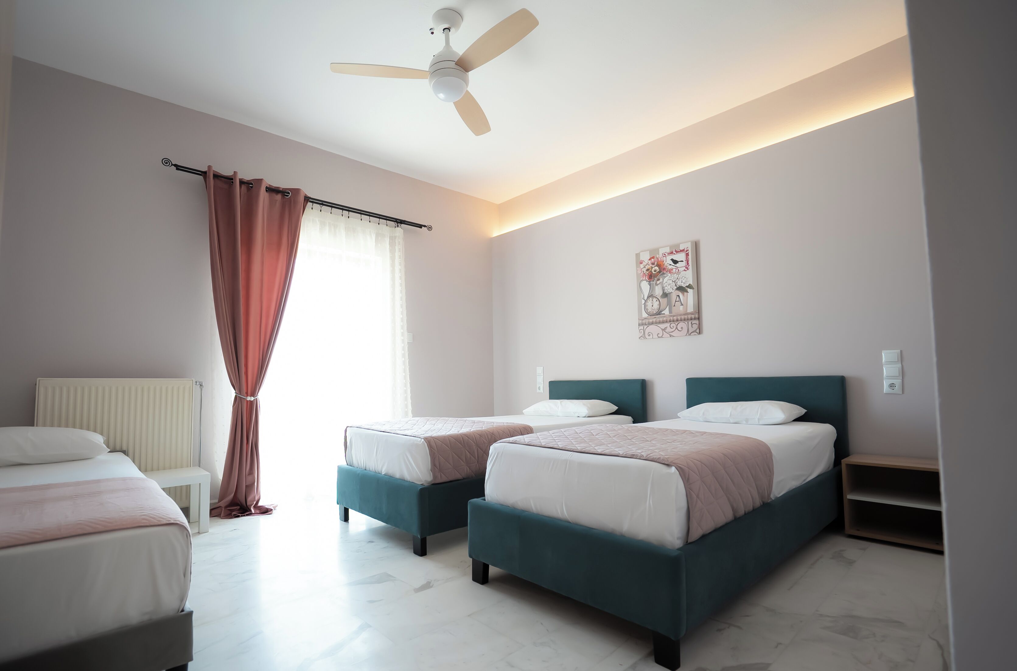 A bedroom with two beds, a ceiling fan, a radiator, and a bedside table.