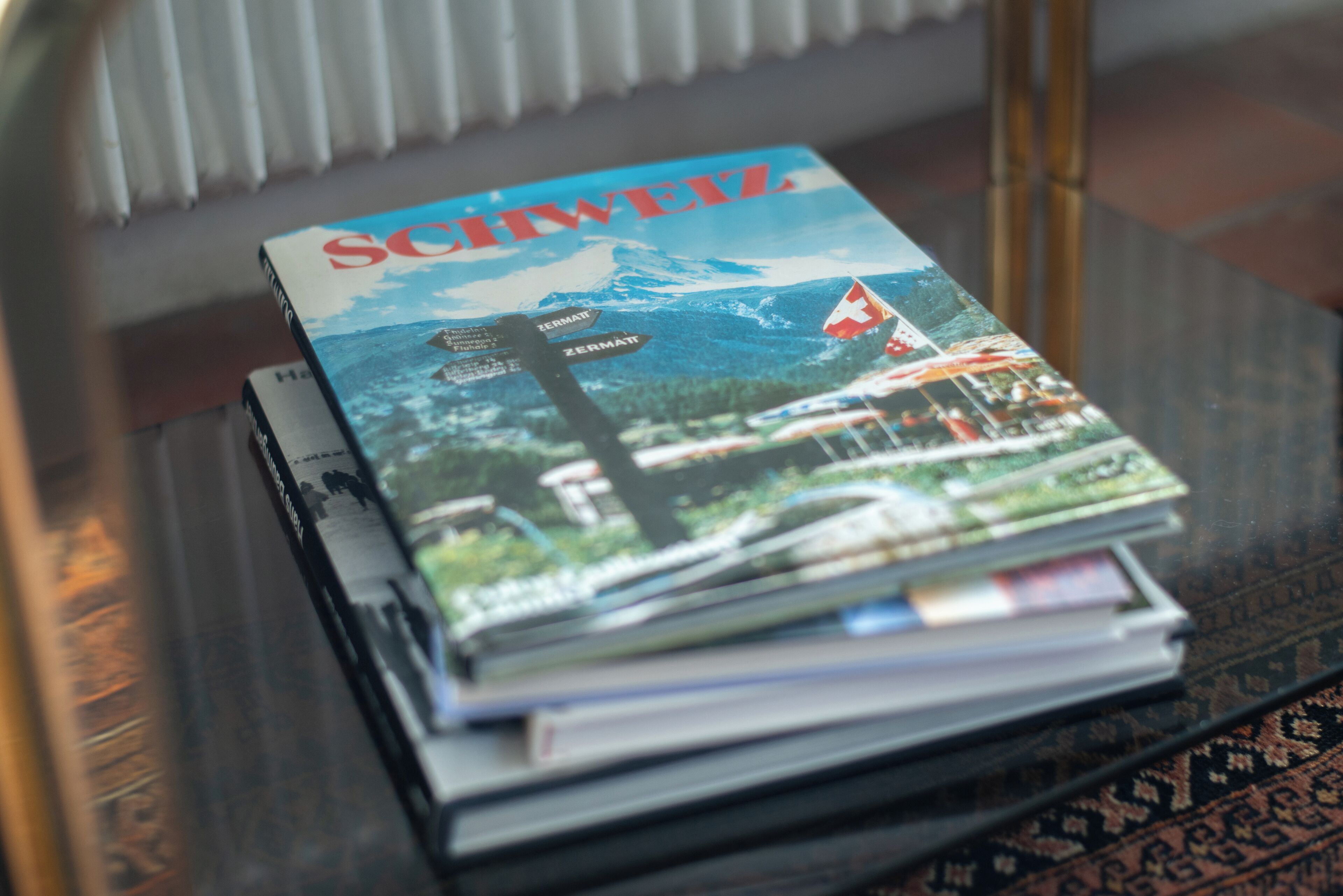 Een stapel tijdschriften op een glazen tafel, met uitzicht op een berg en een vlag.