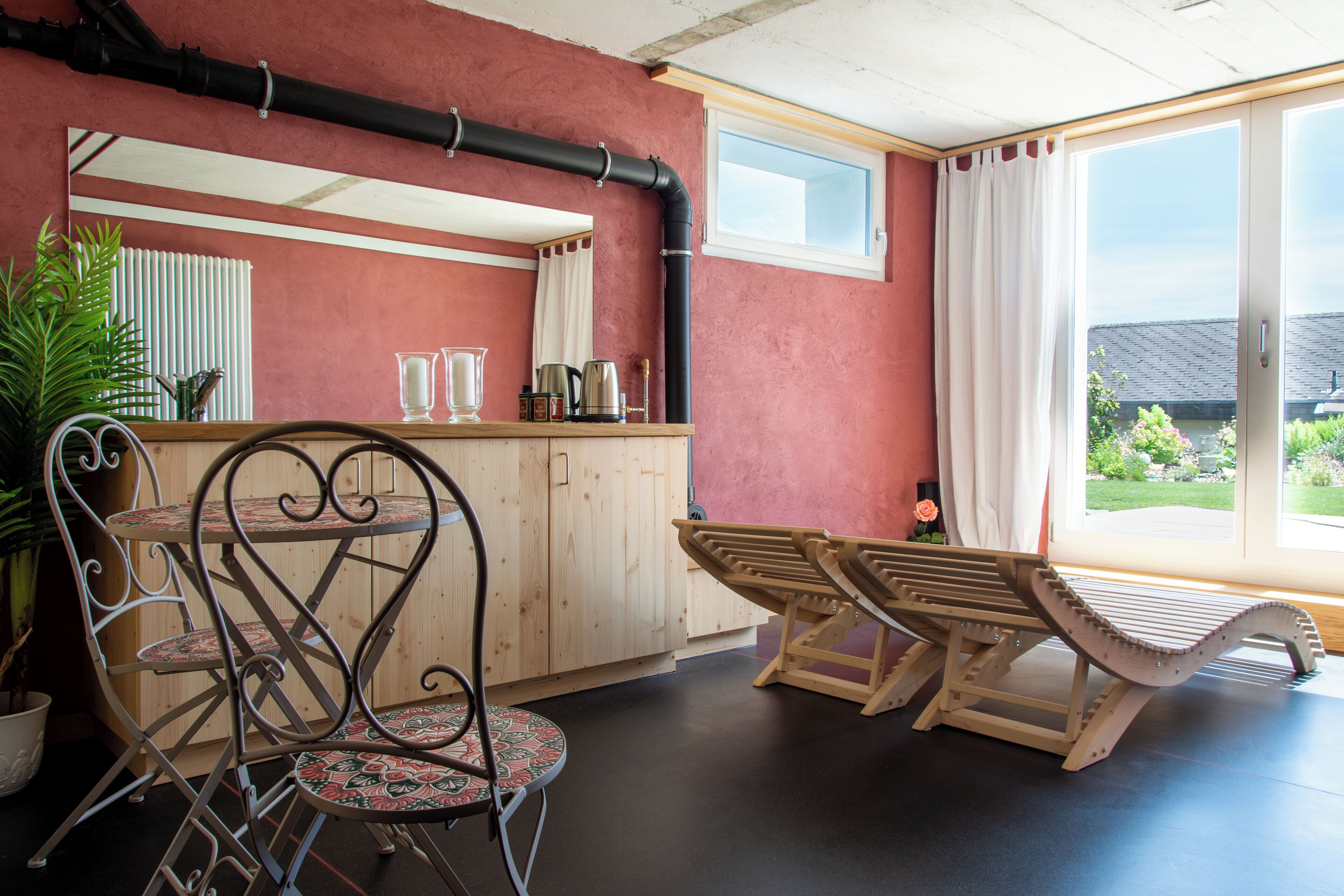 Ein Zimmer mit Holztisch und -stühlen, einer Topfpflanze und einem Fenster mit Blick ins Freie.