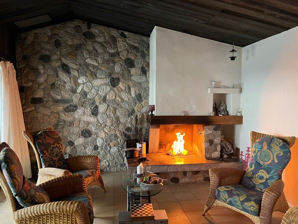 Una sala de estar acogedora con pared de piedra, muebles de mimbre, chimenea y una mesa a cuadros.