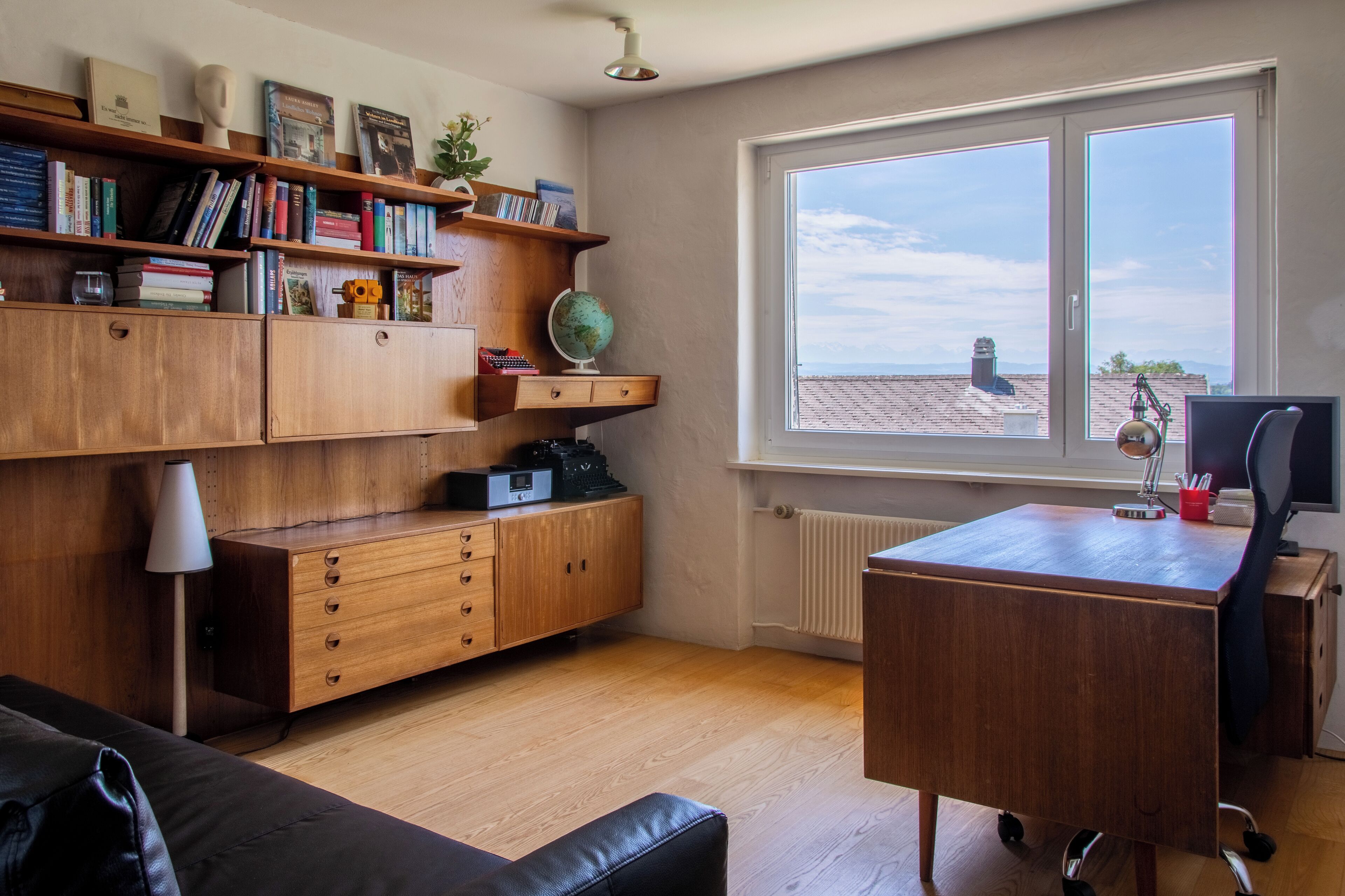 A study room with wooden furniture, a desk, a chair, a globe, bookshelves, and a window with a view of buildings.