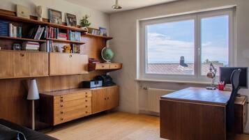 A study room with wooden furniture, a desk, a chair, a globe, bookshelves, and a window with a view of buildings.