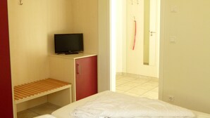 Une chambre d’hôtel avec un lit, un téléviseur posé sur un meuble, une armoire rouge et une étagère en bois.