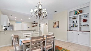 Un coin repas agrémenté d’un lustre, d’un tapis coloré et d’un meuble blanc orné d’objets décoratifs.
