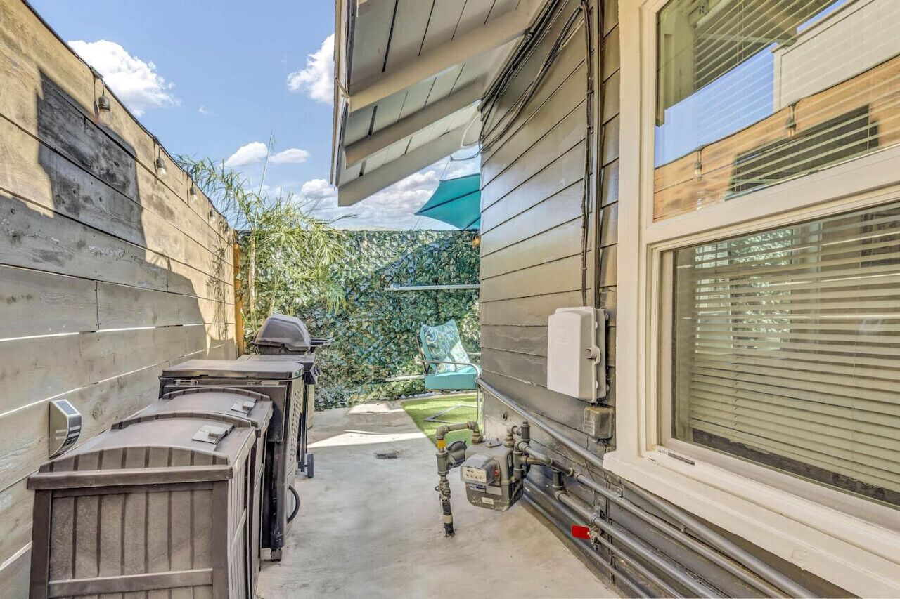 A narrow outdoor corridor with a concrete floor, a blue umbrella, and a chair.