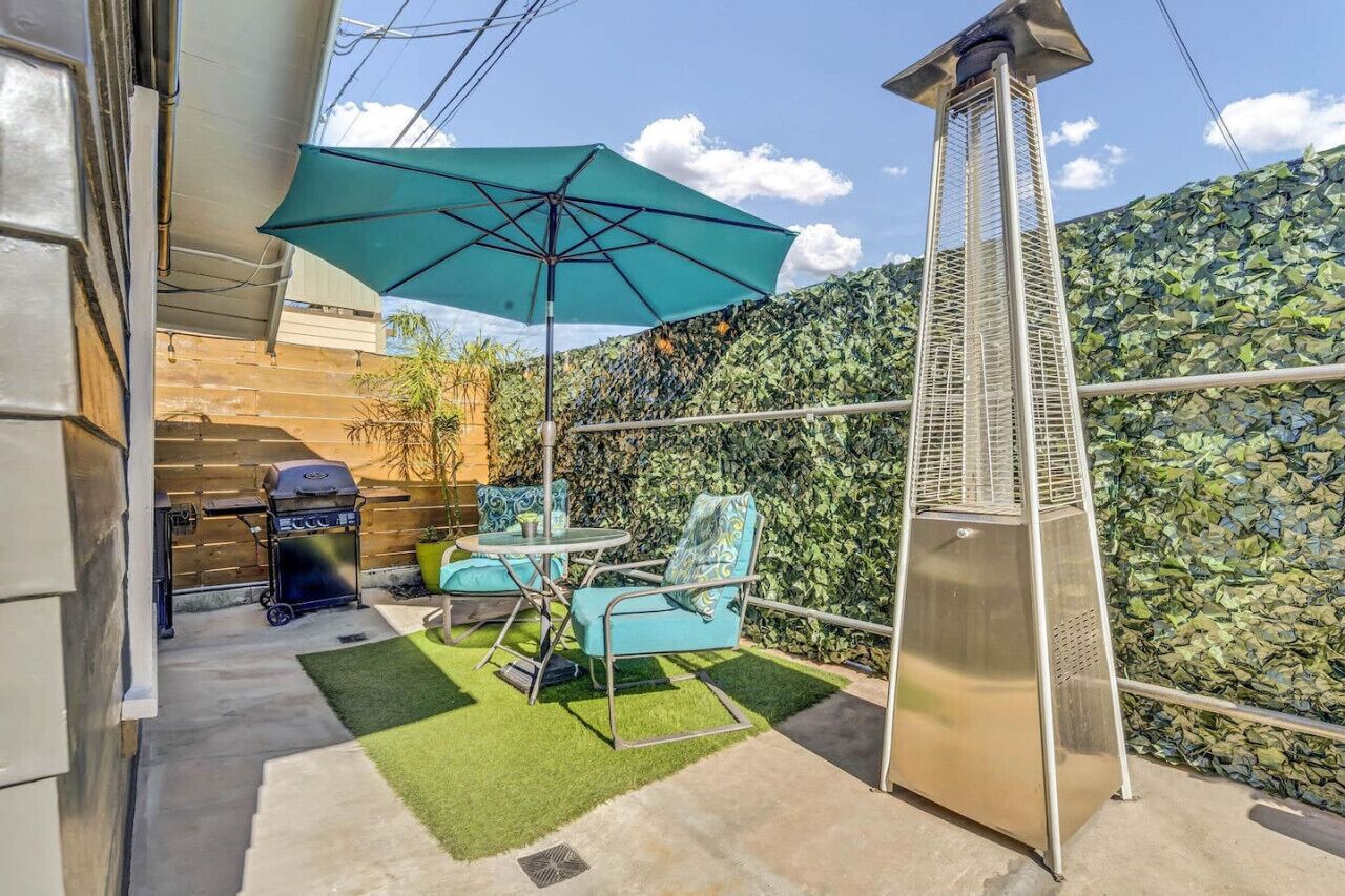 Un patio con una parrilla, asientos exteriores y un paraguas decorativo.
