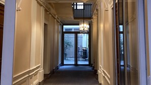 Een gang met betegelde vloer, een glazen deur naar buiten en een decoratief plafond met een centraal lichtarmatuur.