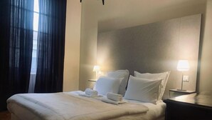 Een netjes opgemaakt bed met witte lakens, twee bedlampen en een houten vloer.