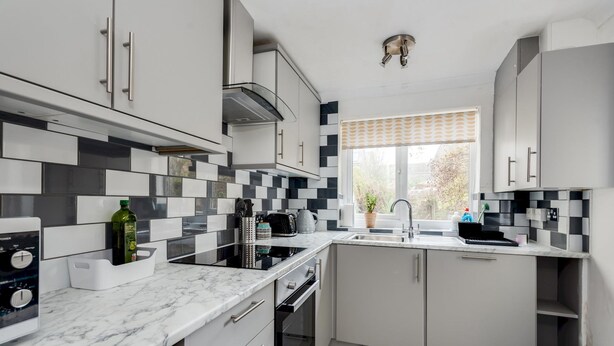 A modern kitchen with grey cabinets, a black and white tiled backsplash, a built-in oven, and a window with a view of trees. - Bright Spacious 2-bedroom Jericho House (Oxford)