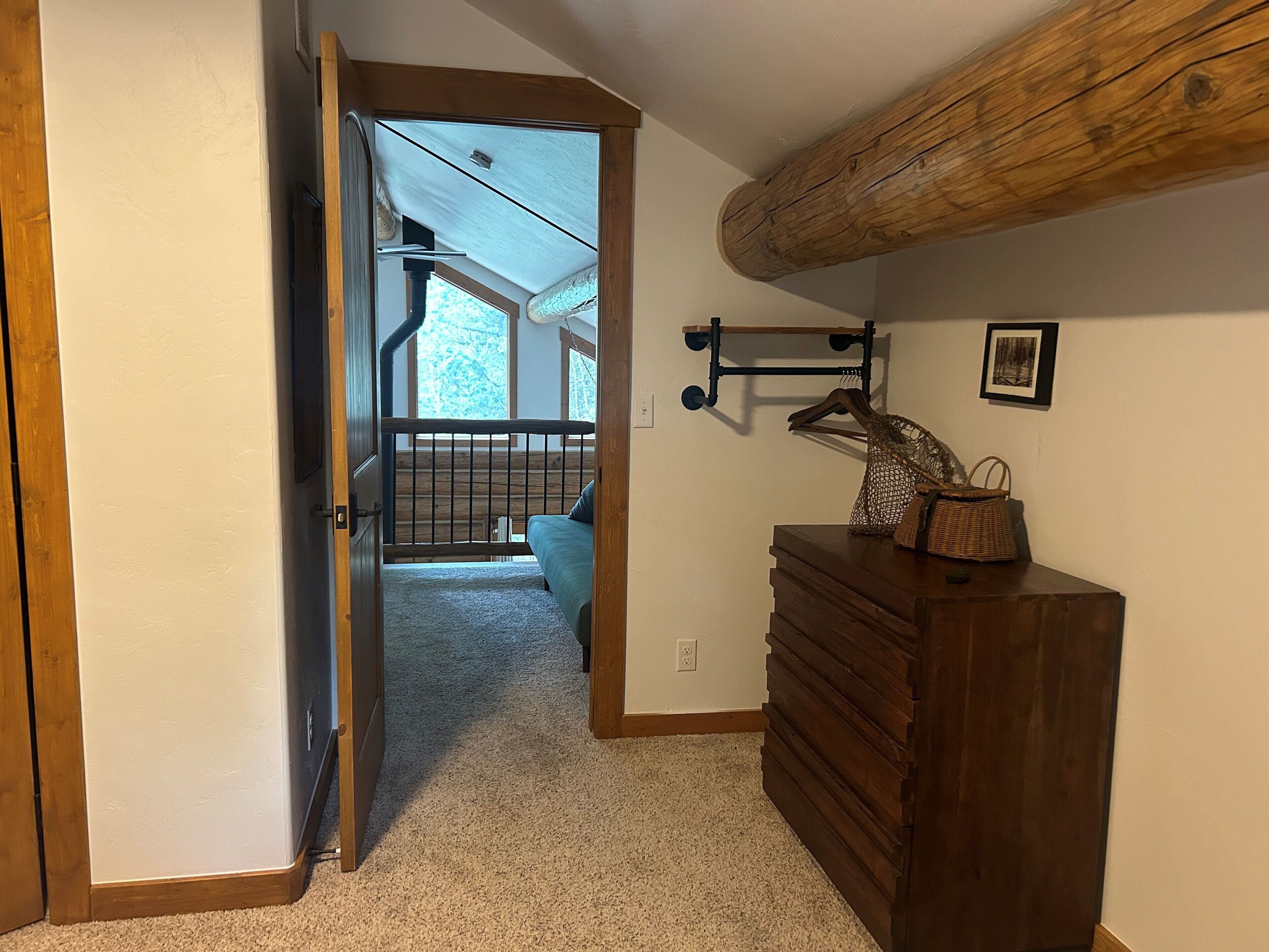 A room with a wooden dresser, a hanging rack, and a view of a balcony with a railing.